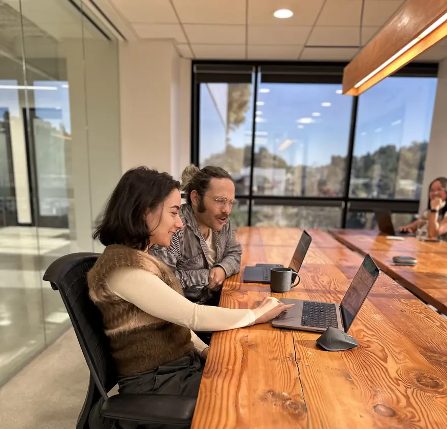 Two Pirros teammates working side by side at a long wooden desk in the office