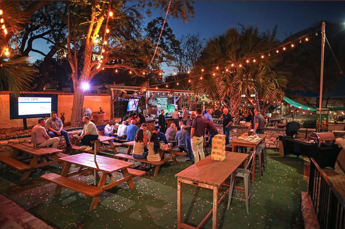Texas River Bar lawn patio at night with picnic tables, palm trees and string lights overhead
